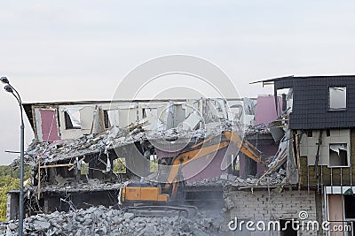 An excavator demolishes a multi-storey building with a ladle. Technique destroys the building, is fittings, concrete and stones. Stock Photo